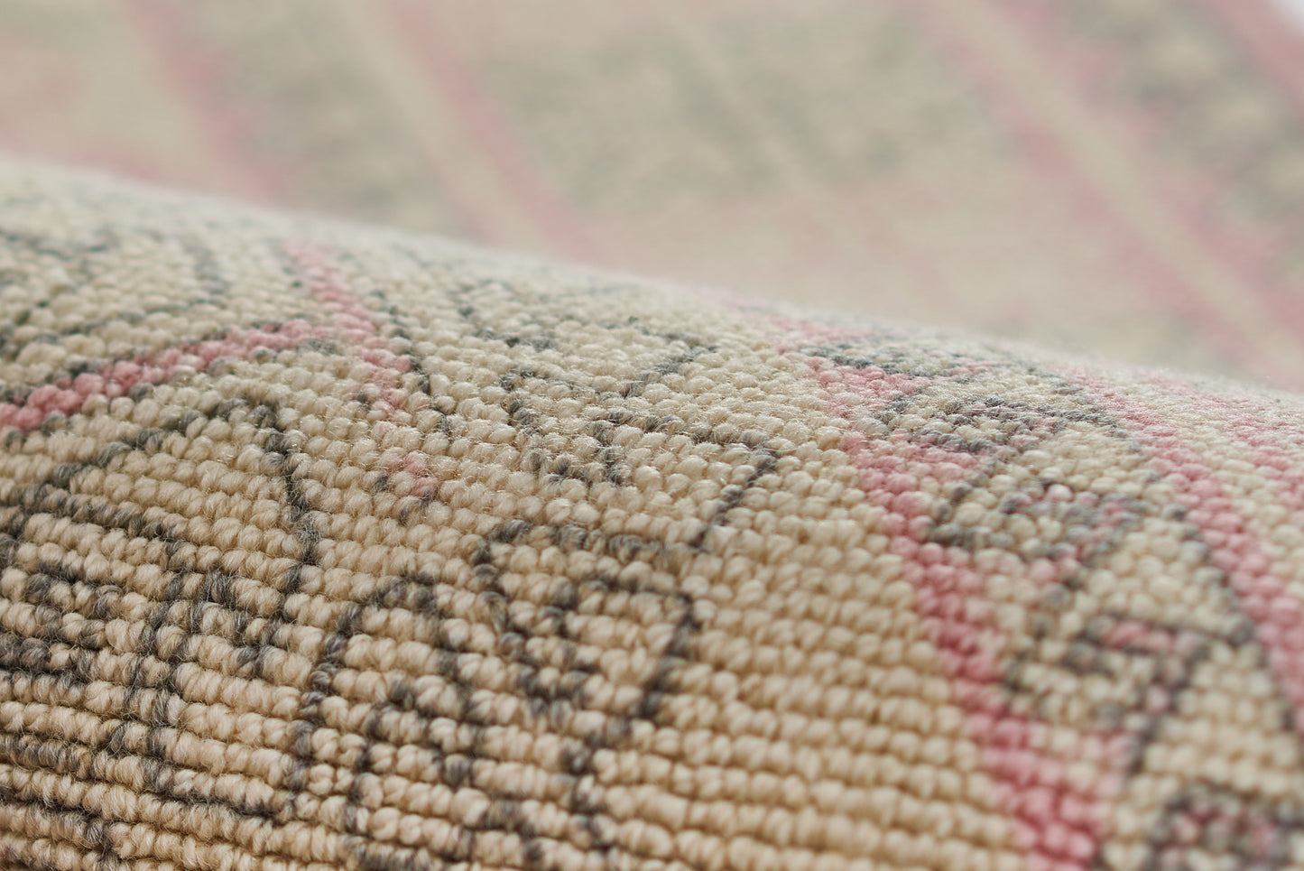 Close-up of a woven kilim rug in beige, taupe and pink with geometric motifs and chunky texture.