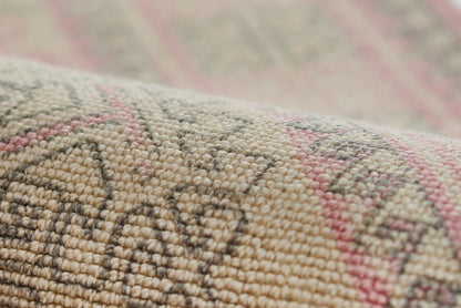 Close-up of a woven kilim rug in beige, taupe and pink with geometric motifs and chunky texture.