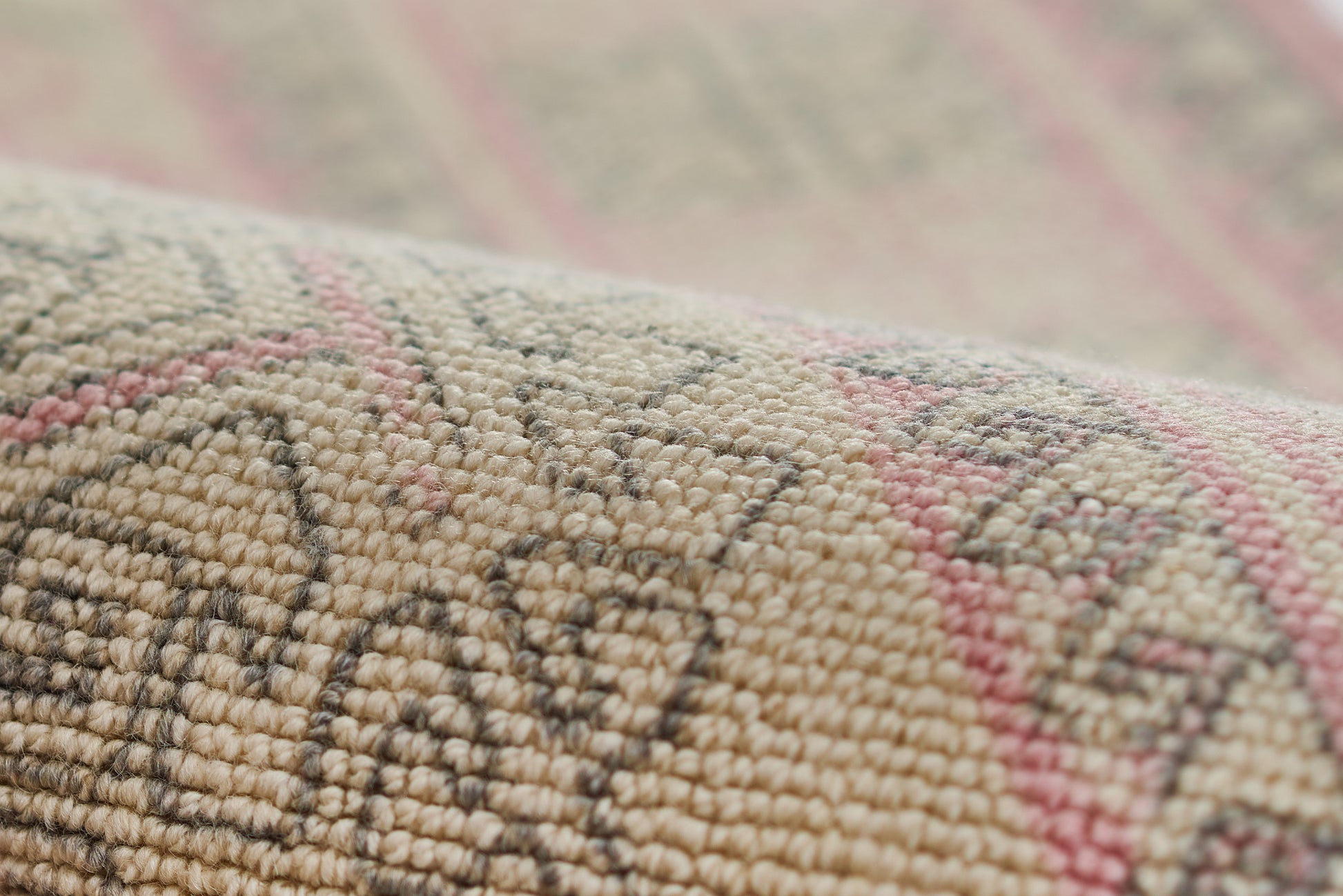 Close-up of a beige woven rug with geometric tribal pattern in pink and taupe, soft wool texture