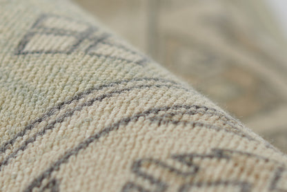 Close-up of beige woven rug with geometric diamond & stripe pattern; textured textile fibers.
