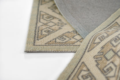 Beige woven rug with brown geometric tribal motifs; folded edge reveals textured weave.
