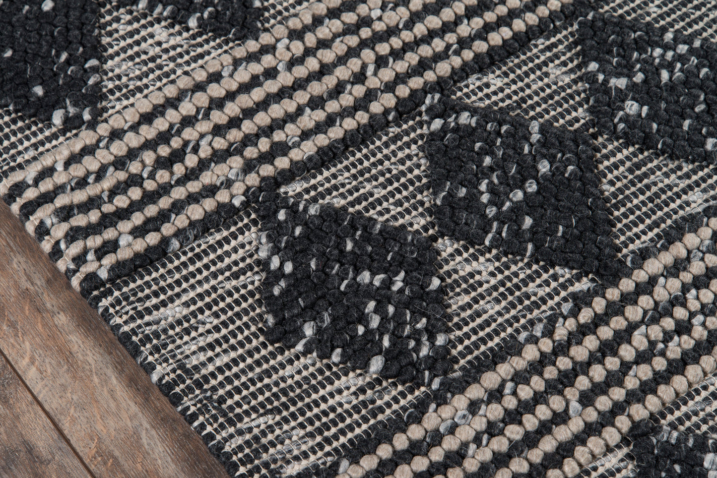 Close-up of Andesand woven rug: black and beige geometric diamond pattern with looped texture on wood floor.