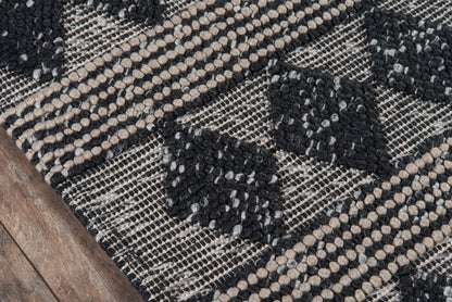 Handwoven rug with black diamond motifs on natural beige, dotted border and chunky weave.
