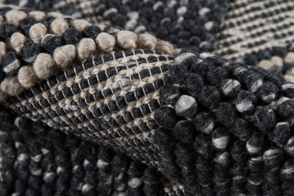 Close-up view of a chunky woven rug in black, charcoal and beige with looped pom-pom tufts