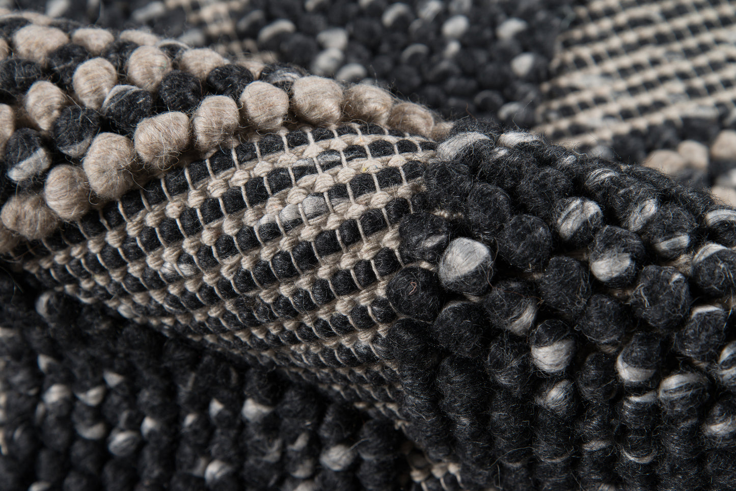 Close-up of a chunky woven rug with black, gray & beige looped fibers & braided texture.