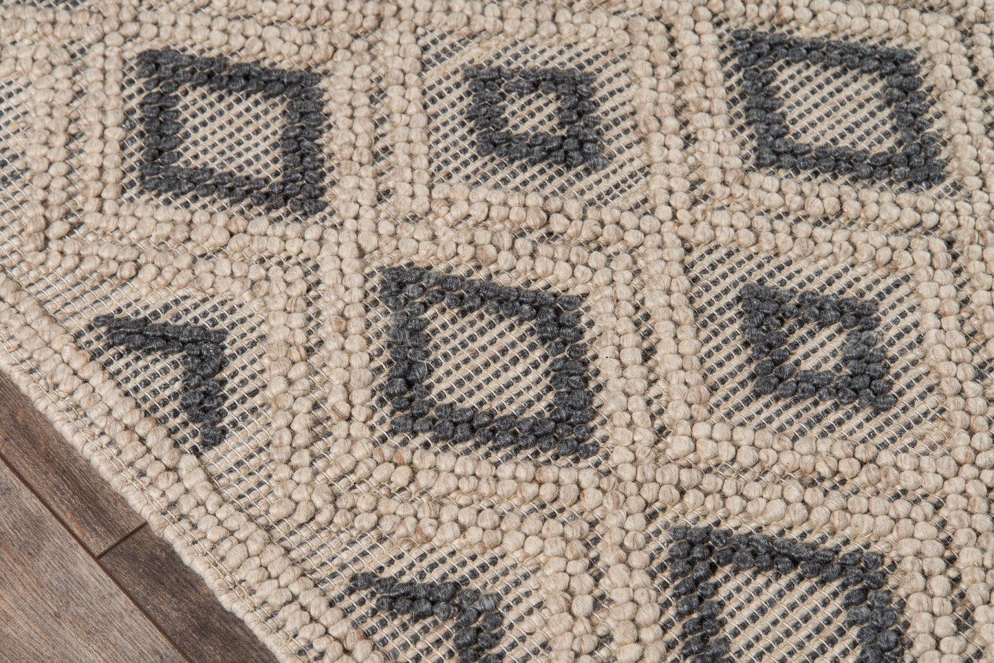 Beige chunky woven rug with dark charcoal diamond motifs & geometric grid; textured loop pile on wood floor.