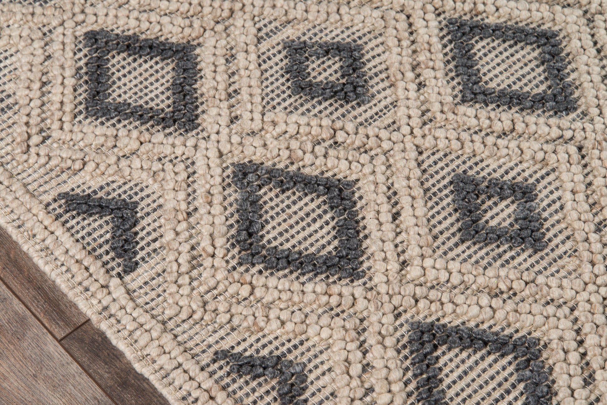 Beige geometric rug with black square diamond motifs; chunky loop texture on wooden floor.