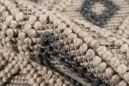 Close-up of a beige & charcoal woven rug with looped boucle texture & a geometric dotted pattern.
