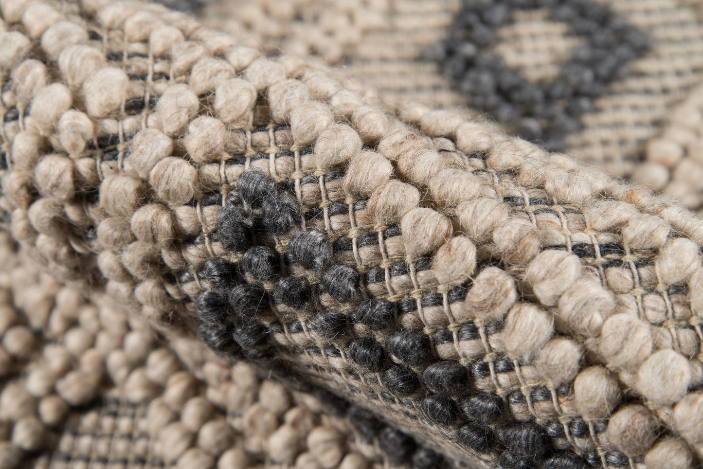 Close-up of beige boucle rug with chunky woven texture & black dot motif.
