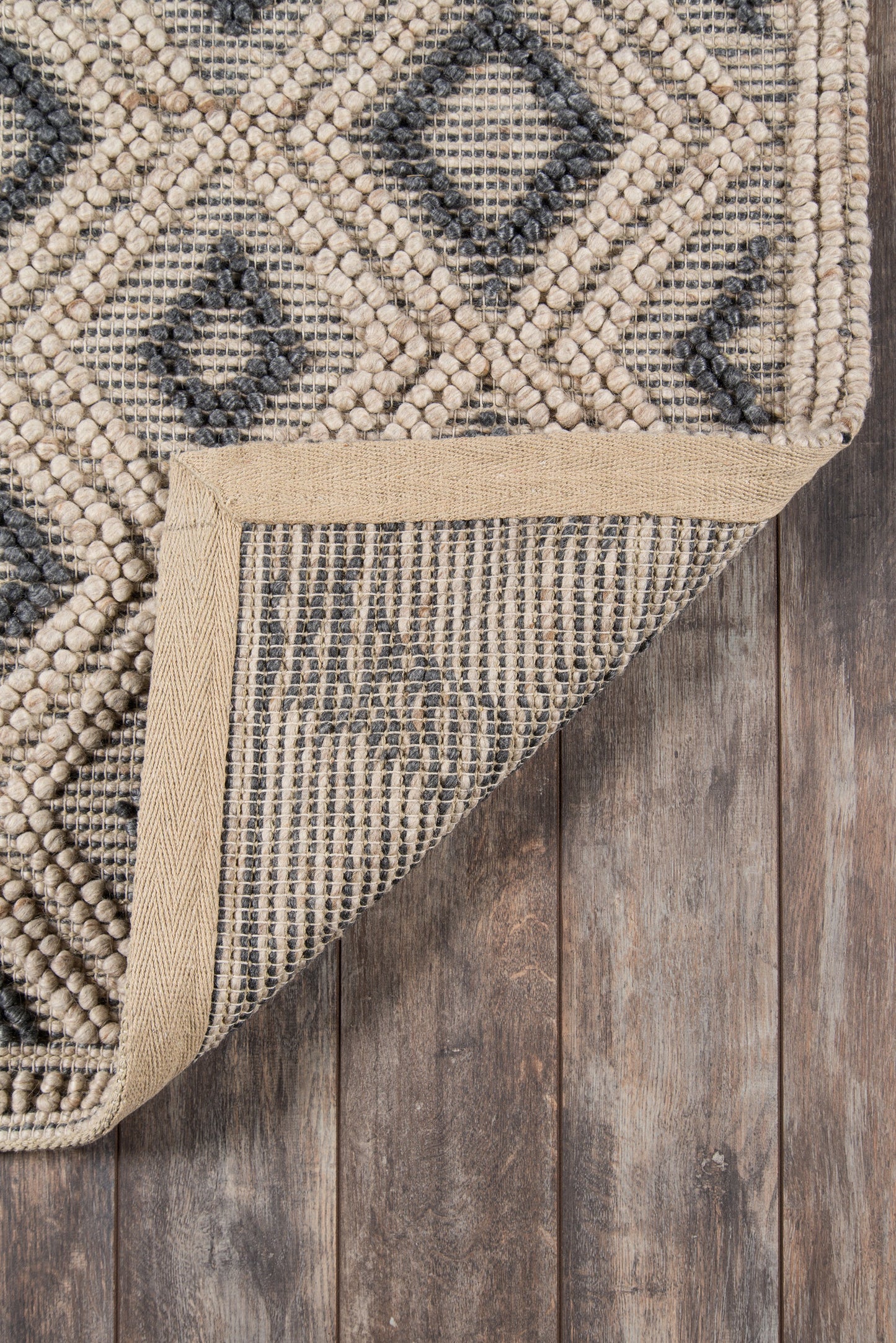 Geometric beige and navy area rug with diamond motif; woven texture, corner folded to show natural backing on wood floor.