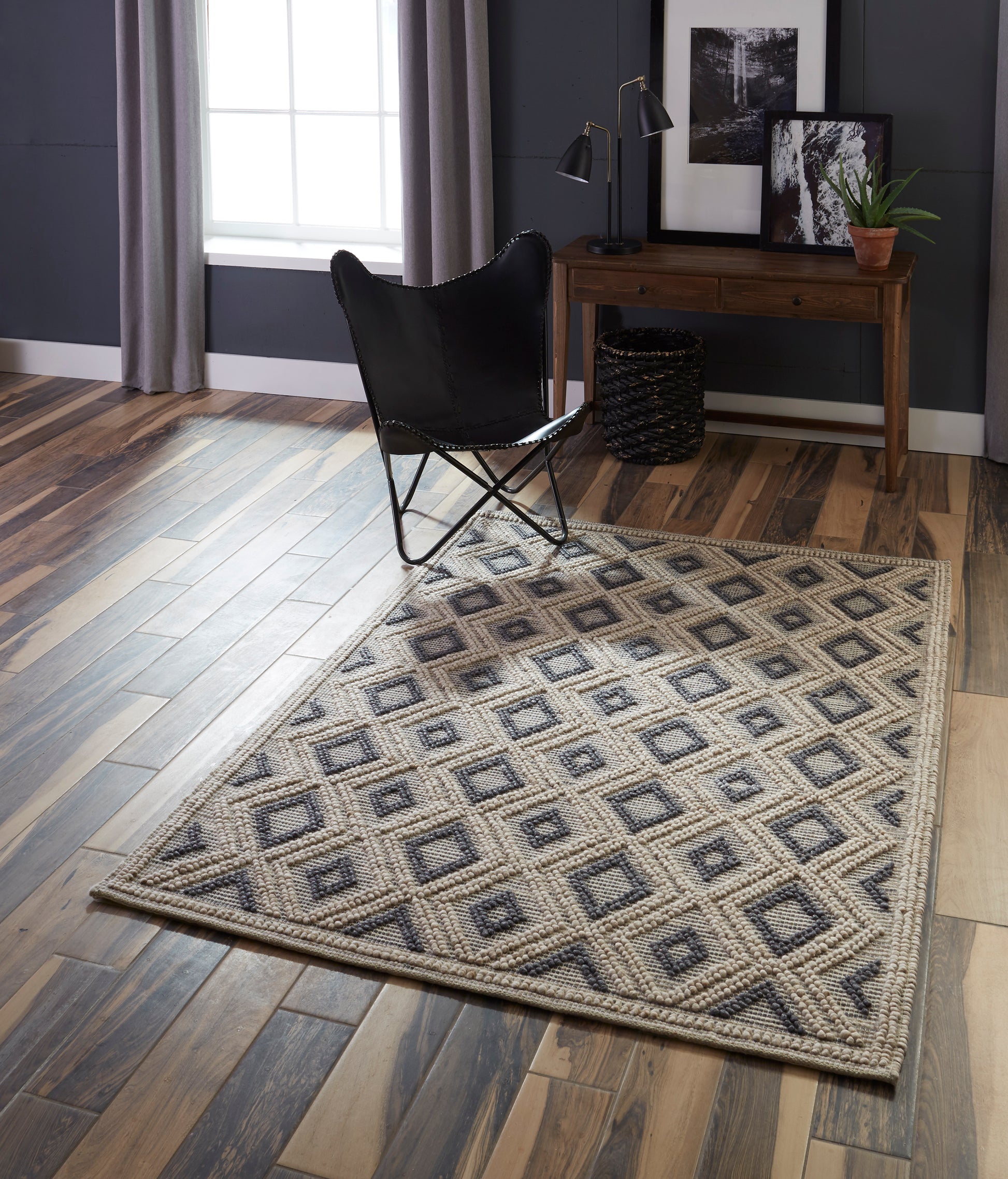Geometric diamond woven rug in beige and navy on a wood floor, paired with a black butterfly chair and wooden desk.