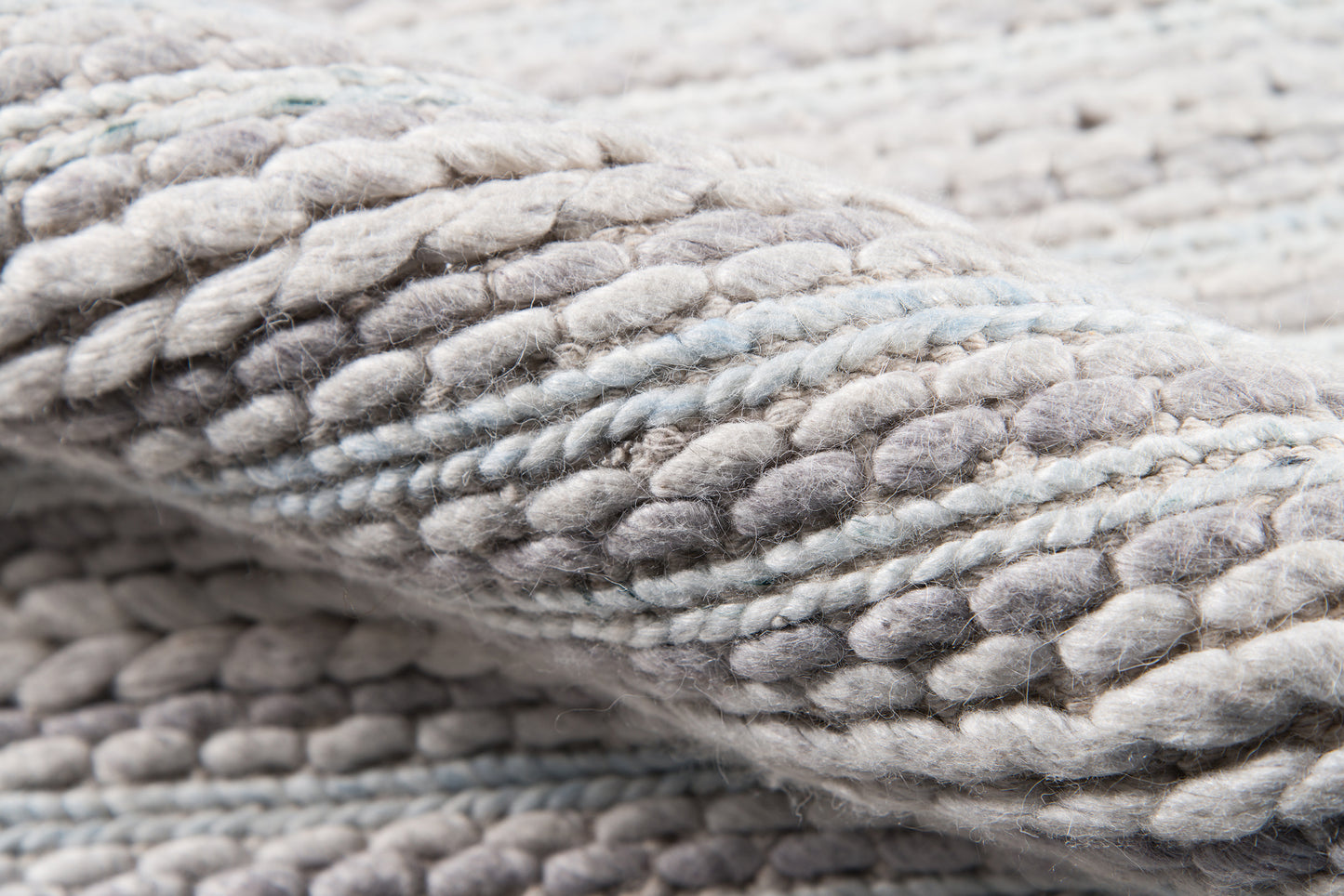 Close-up of chunky gray knit yarn with pale blue accents; soft, thick knitted throw blanket texture.
