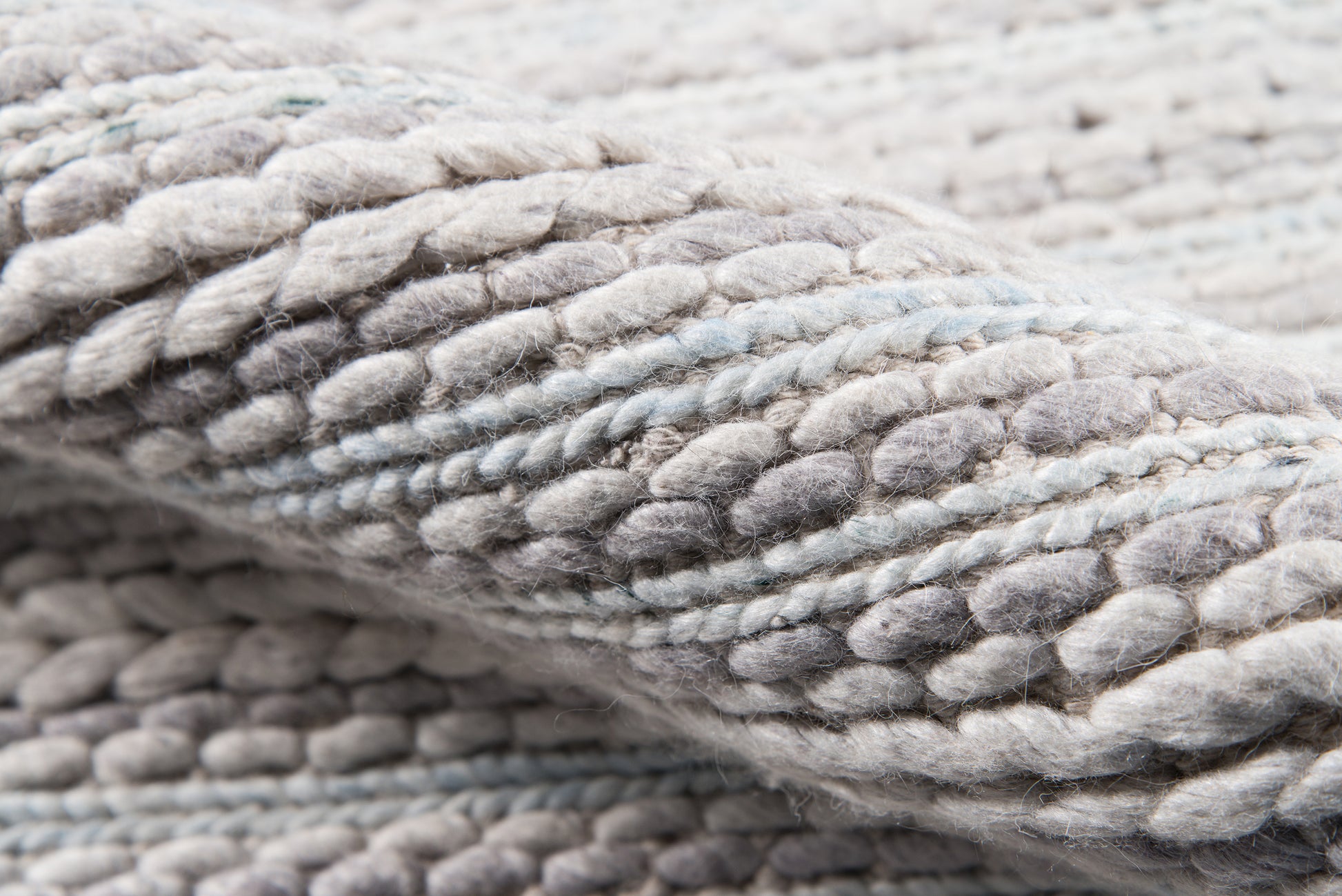 Close-up of chunky gray knit yarn with pale blue accents; soft, thick knitted throw blanket texture.