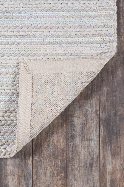 Light gray textured rug with chunky weave; corner folded to reveal beige backing on dark wood floor.