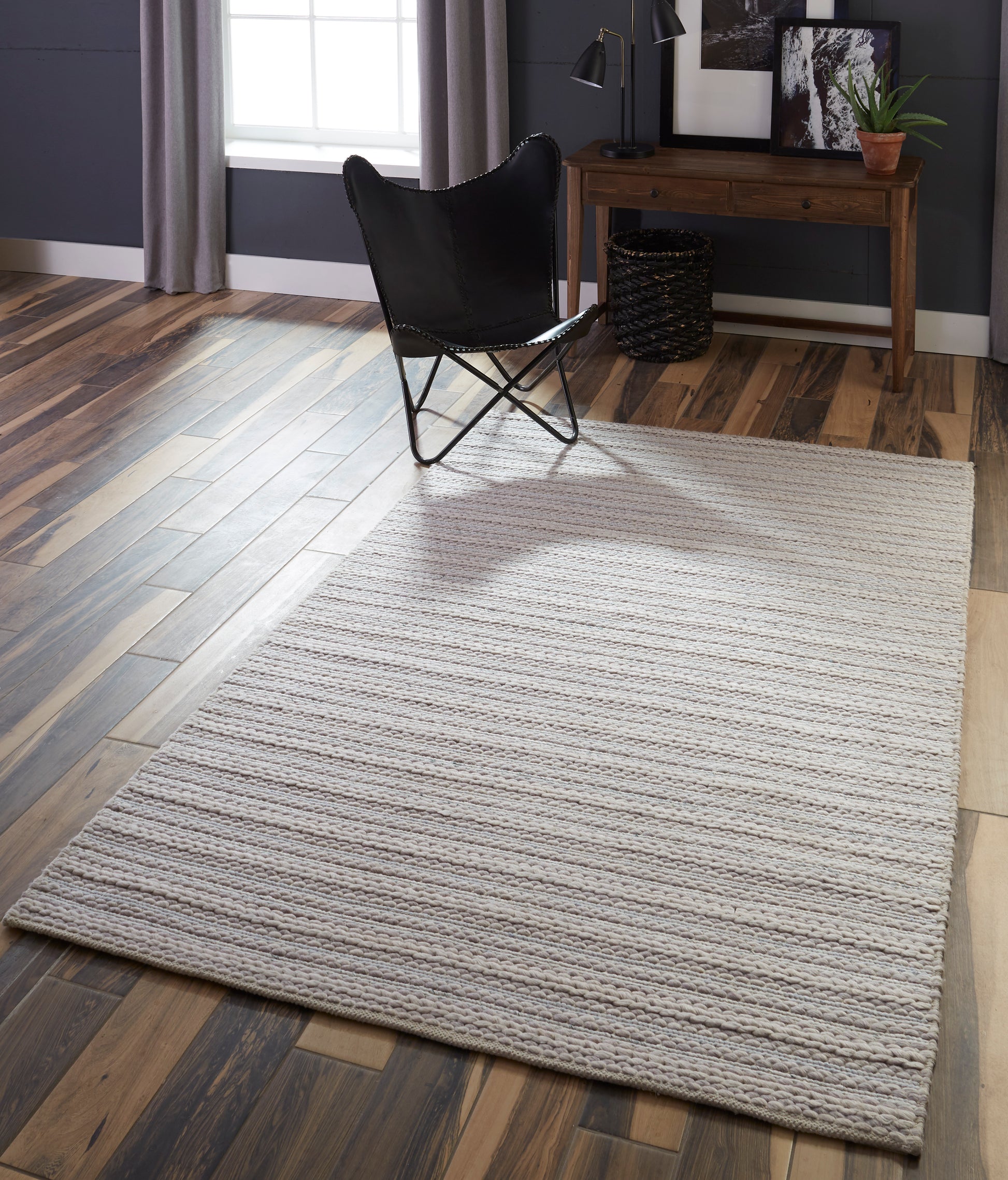 Rectangular light gray striped area rug on wood floor with a black butterfly chair and wooden console table in a modern living room.
