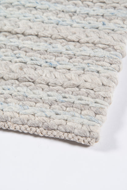 Beige chunky woven rug with pale blue specks; thick rope-like yarn, visible edge.