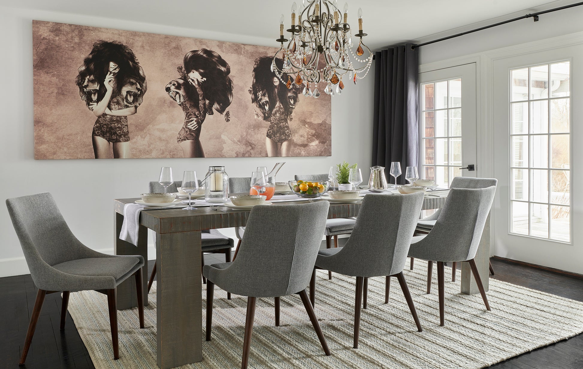 Modern dining room with a grey 6' x 9' rug under a wooden dining table, grey upholstered chairs, crystal chandelier, and sepia-toned wall art.