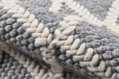 Close-up of a chunky woven rug in gray and cream with thick looped yarn and striped pattern.