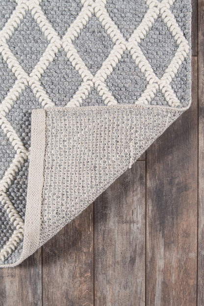Grey and cream geometric rug with diamond lattice, folded corner reveals beige underside on wooden floor.