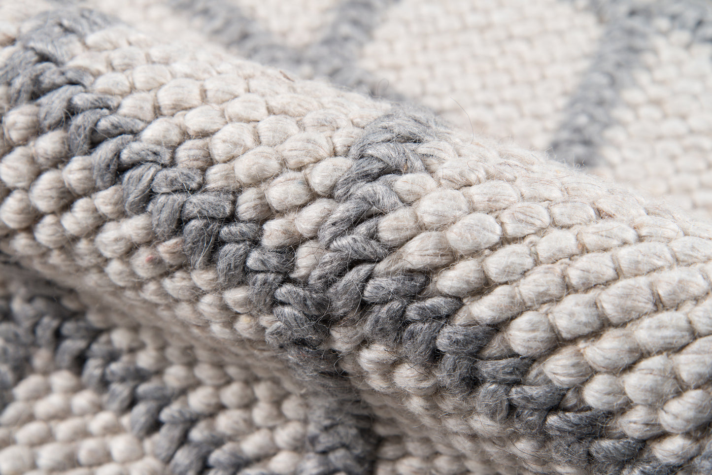 Chunky knit rug in cream and gray tones, thick woven wool with soft, textured loops.