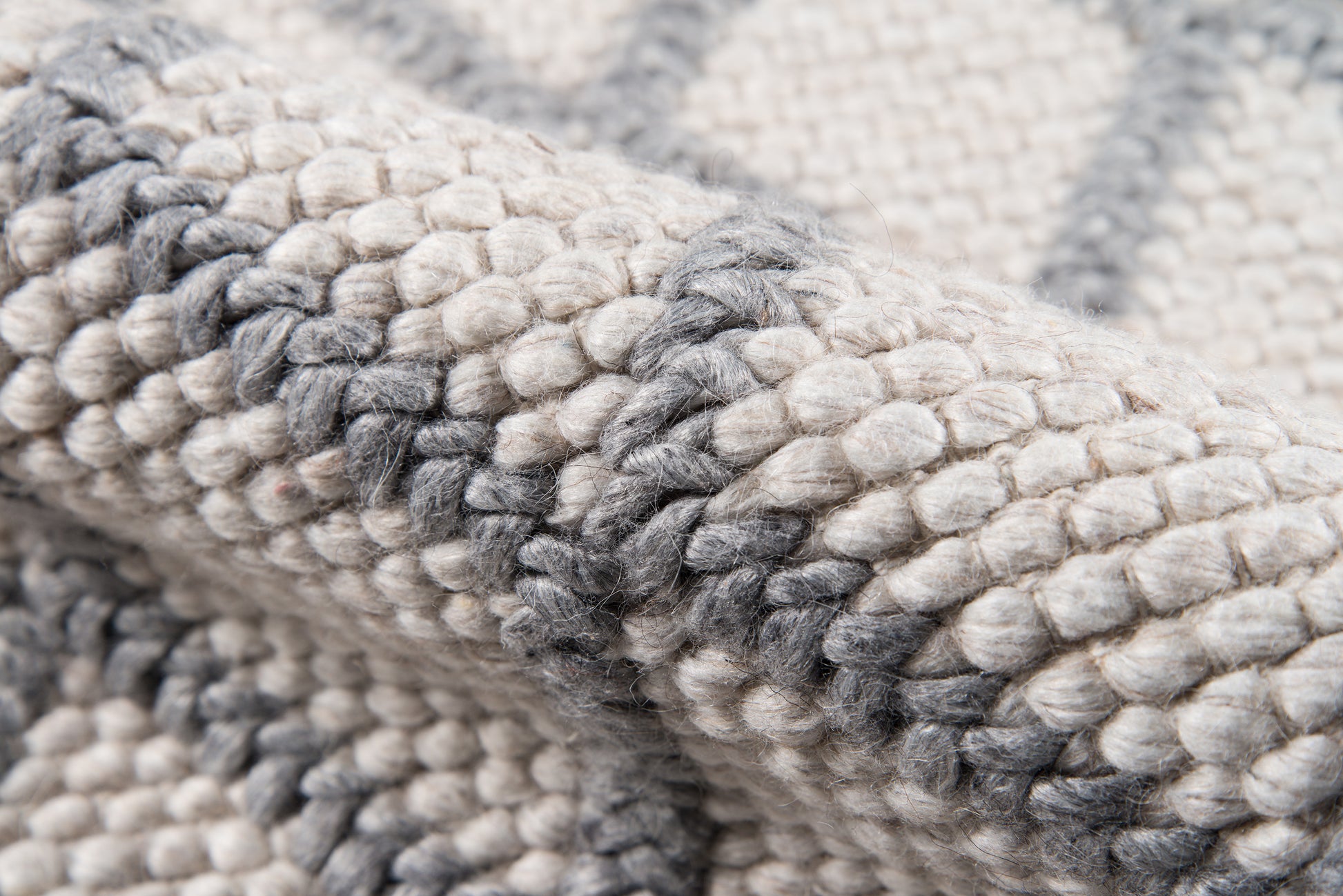 Chunky knit rug in cream and gray tones, thick woven wool with soft, textured loops.