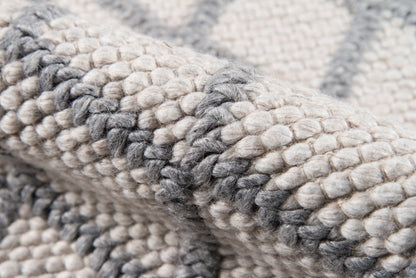 Chunky knit rug in cream and gray tones, thick woven wool with soft, textured loops.