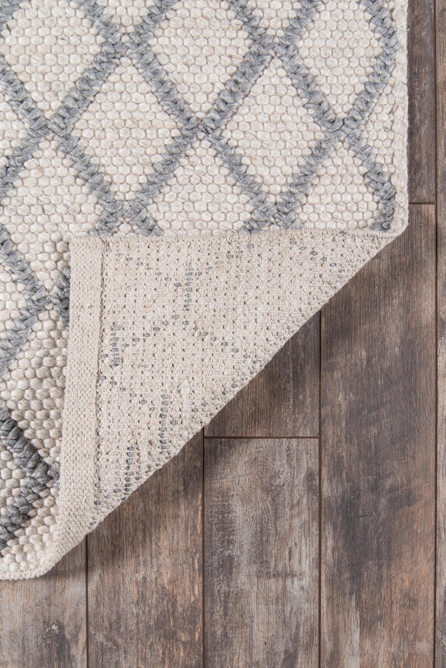 Natural-toned rug with gray diamond lattice pattern, textured weave, folded corner on dark wood floor.