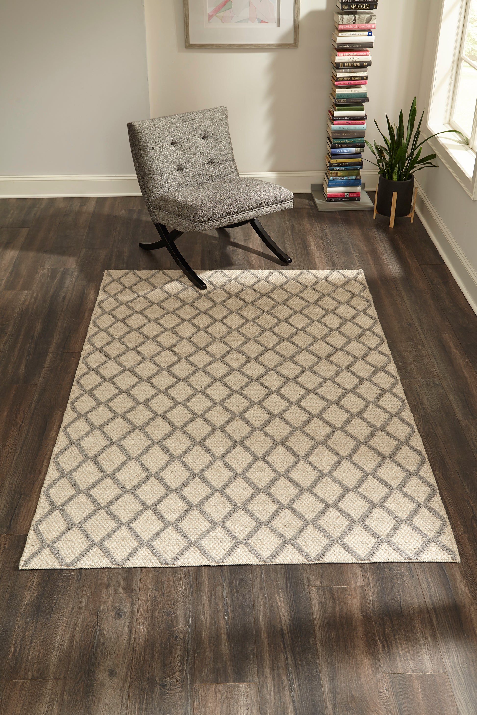 Grey tufted rocking chair beside a sand beige diamond-pattern rug on dark wood floor in a modern living room.