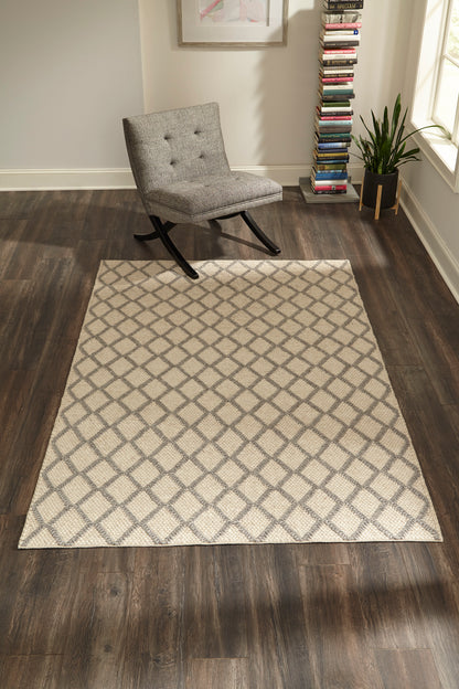 Grey tufted rocking chair beside a sand beige diamond-pattern rug on dark wood floor in a modern living room.