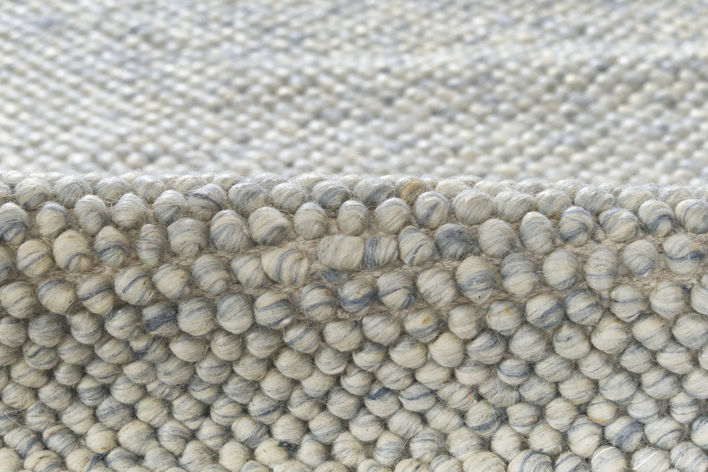 Close-up of a grey-blue boucle rug with dense looped pile; textured, cozy, modern home decor.