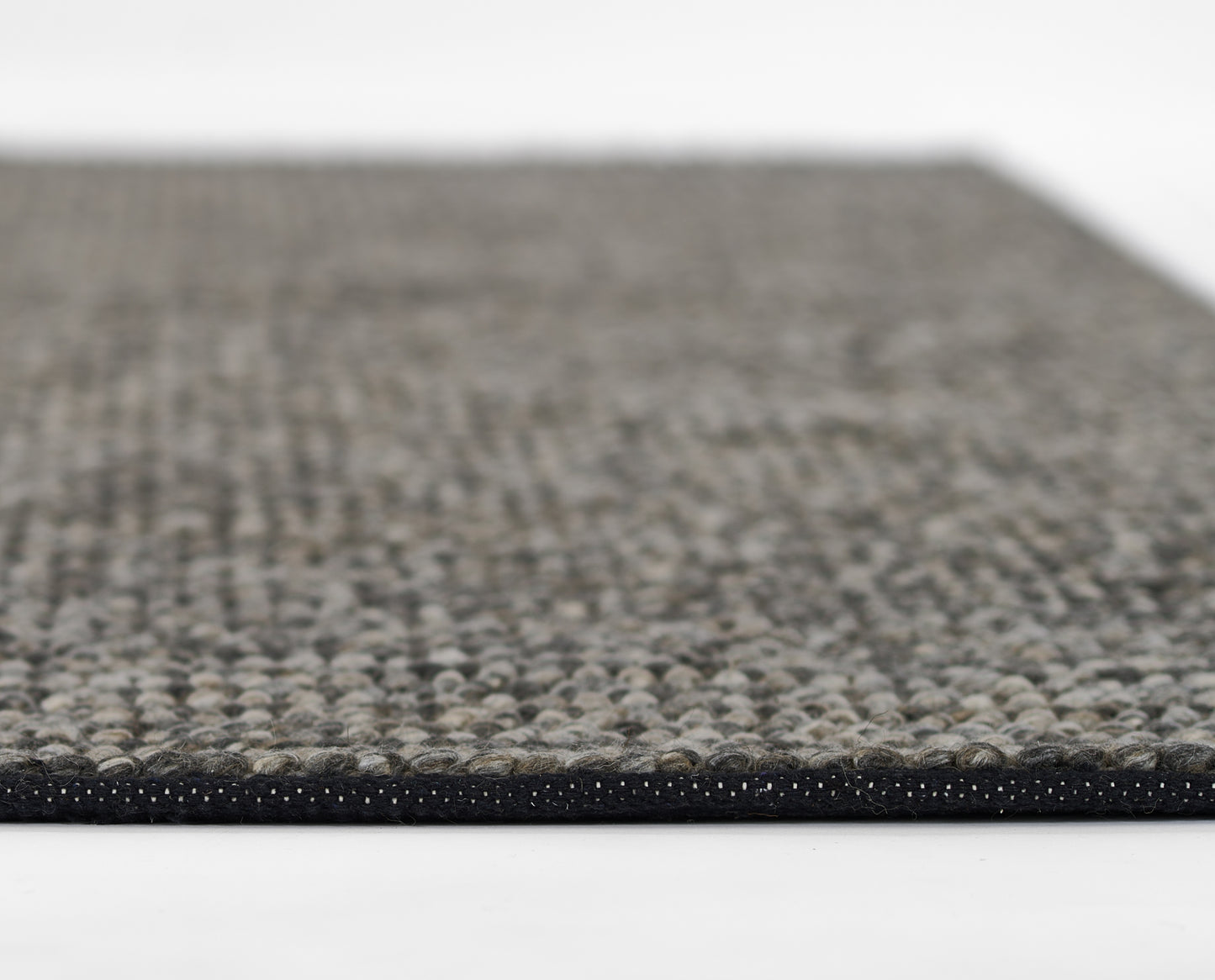 Close-up of a grey-beige speckled woven rug with a black edge binding.