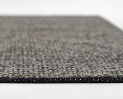 Close-up of a gray speckled boucle-style woven rug with a black edge binding.