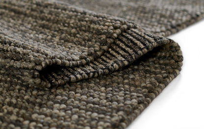 Close-up of a textured brown boucle rug with loop pile and folded edge in taupe-gray tones.