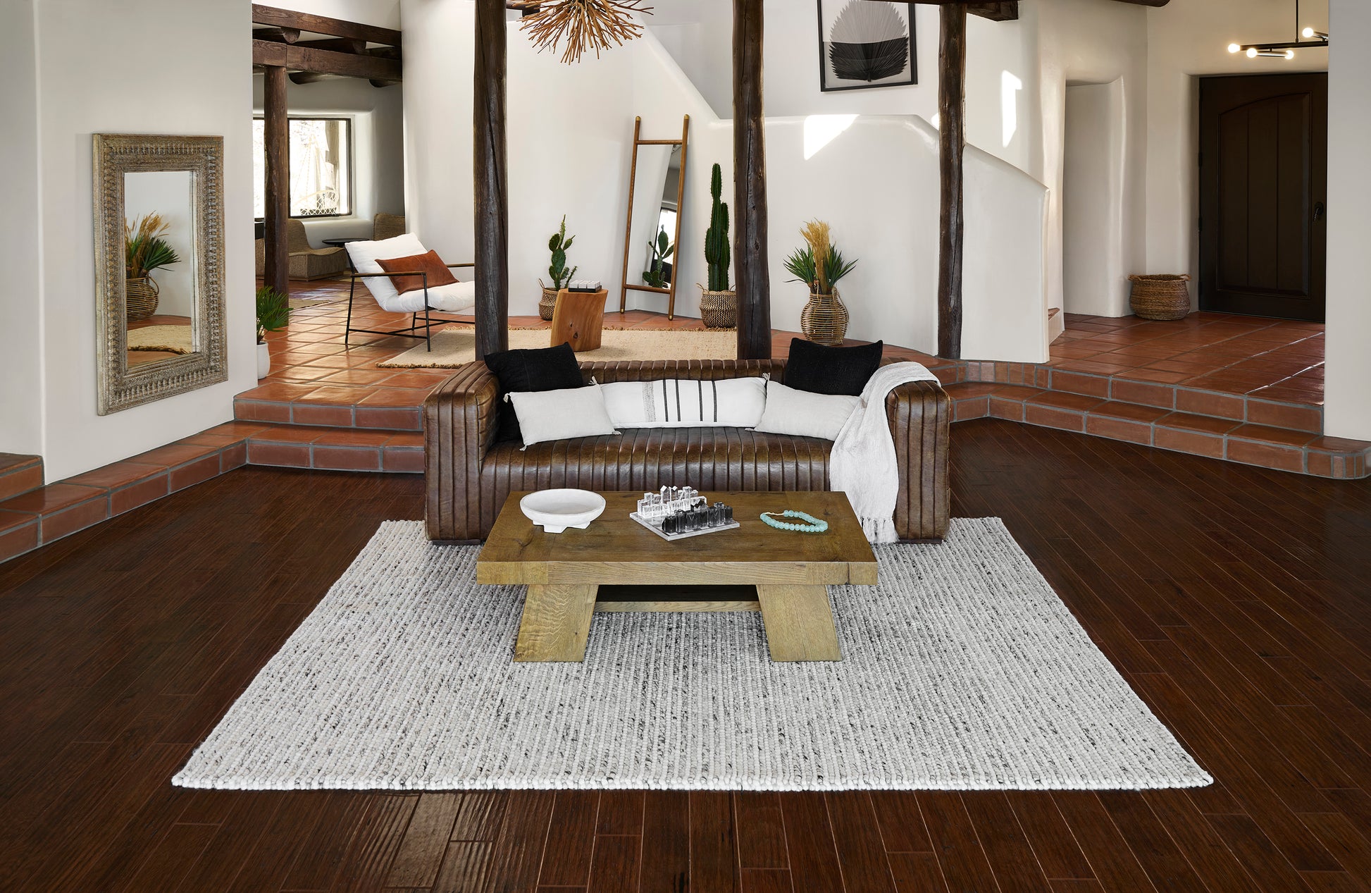 Brown leather sofa with white and black cushions, beige throw, rustic wood coffee table on a light gray rug.
