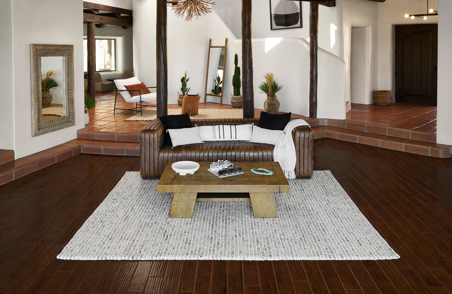 Light gray textured area rug centered under a chunky wooden coffee table in a brown leather sofa living room.