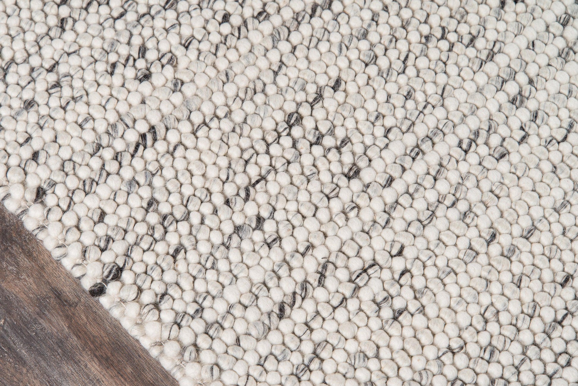 Cream and light gray speckled loop rug with chunky texture on a wooden floor.