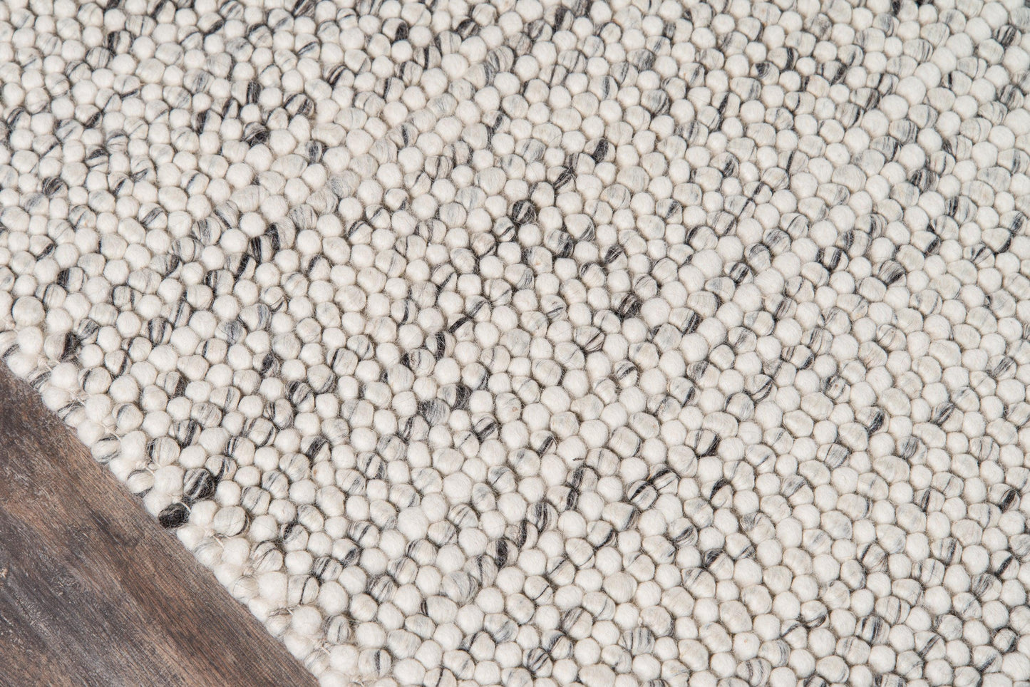 Andes Sand ivory area rug with pebble-like tufts and subtle dark specks on a wood floor.