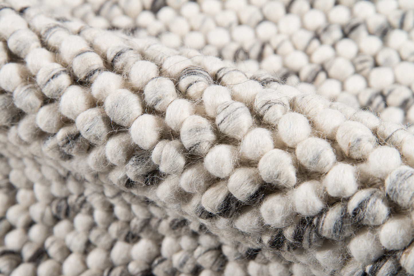 Ivory-gray chunky boucle rug close-up with rounded pom-poms and soft wool texture.
