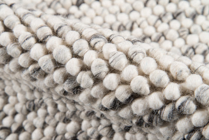 Close-up of ivory & gray boucle knit blanket with chunky pom-pom yarn texture, soft and plush.