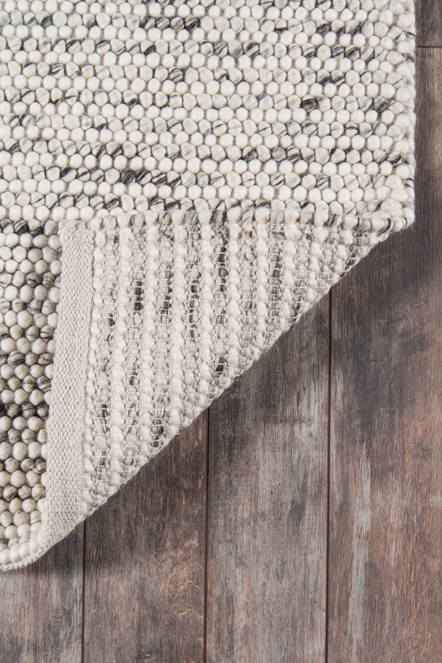 Neutral ivory-beige chunky boucle rug with gray flecks on dark wood floor, folded corner.