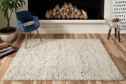 Cream chunky woven area rug with dark flecks on wood floor; blue upholstered chair and stacked firewood by a fireplace.