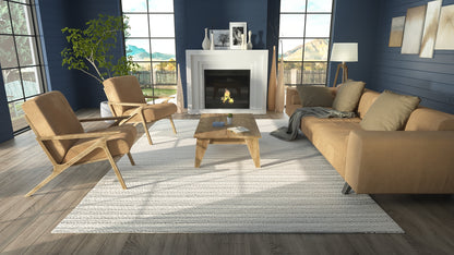 Cozy living room with tan sofa, two mid-century chairs, wooden coffee table, blue walls, large windows, fireplace, light gray rug.