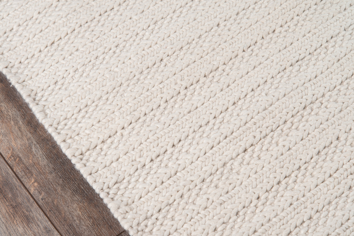 Cream chunky braided rug with thick looped weave on dark wood flooring.