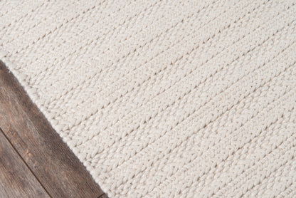 Ivory chunky braided rug on dark wood floor; thick woven texture in neutral cream tones.