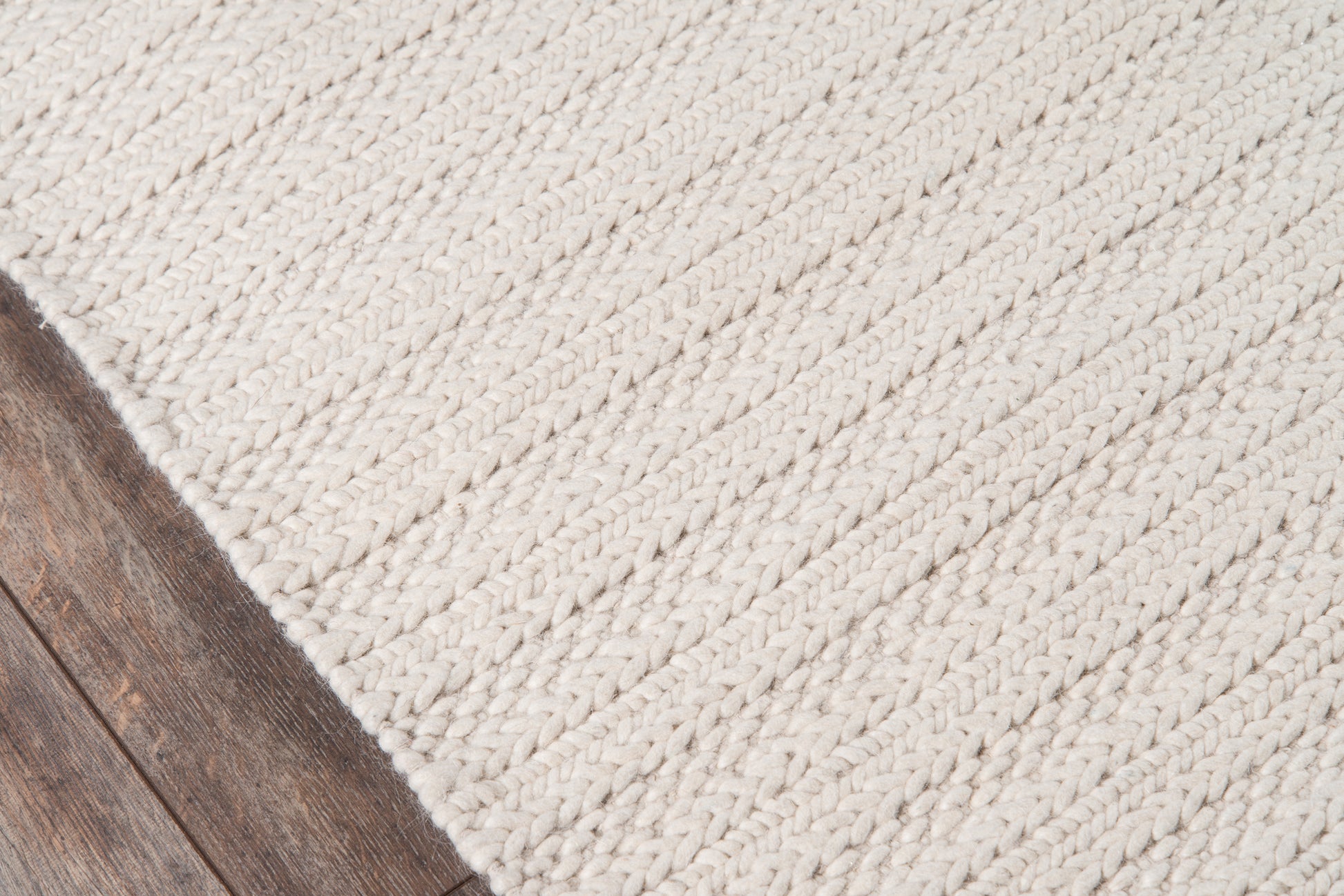 Cream chunky braided rug on dark wood floor, edge visible, casual coastal style.