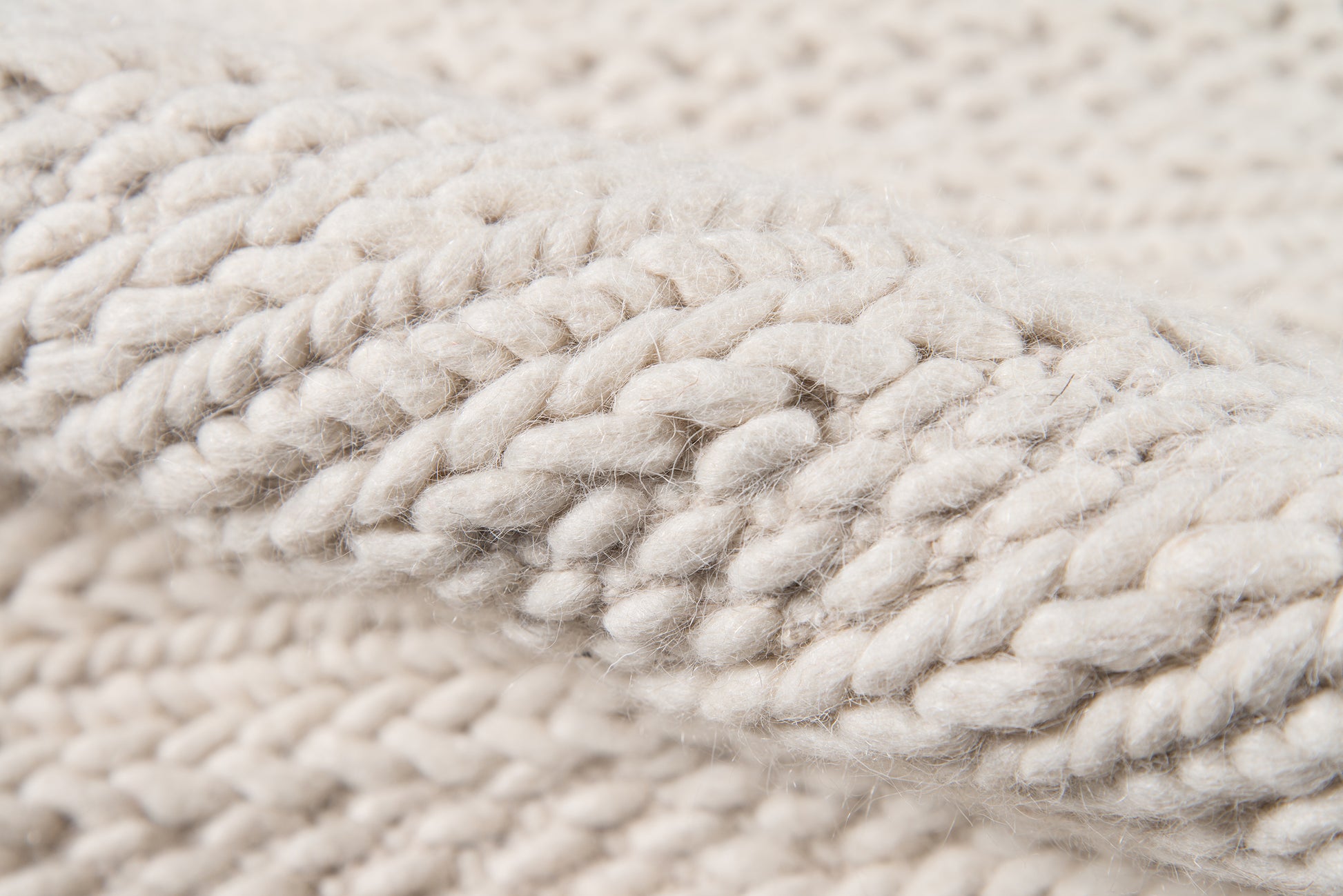Cream chunky yarn close-up with thick twisted cable stitches, soft and cozy.