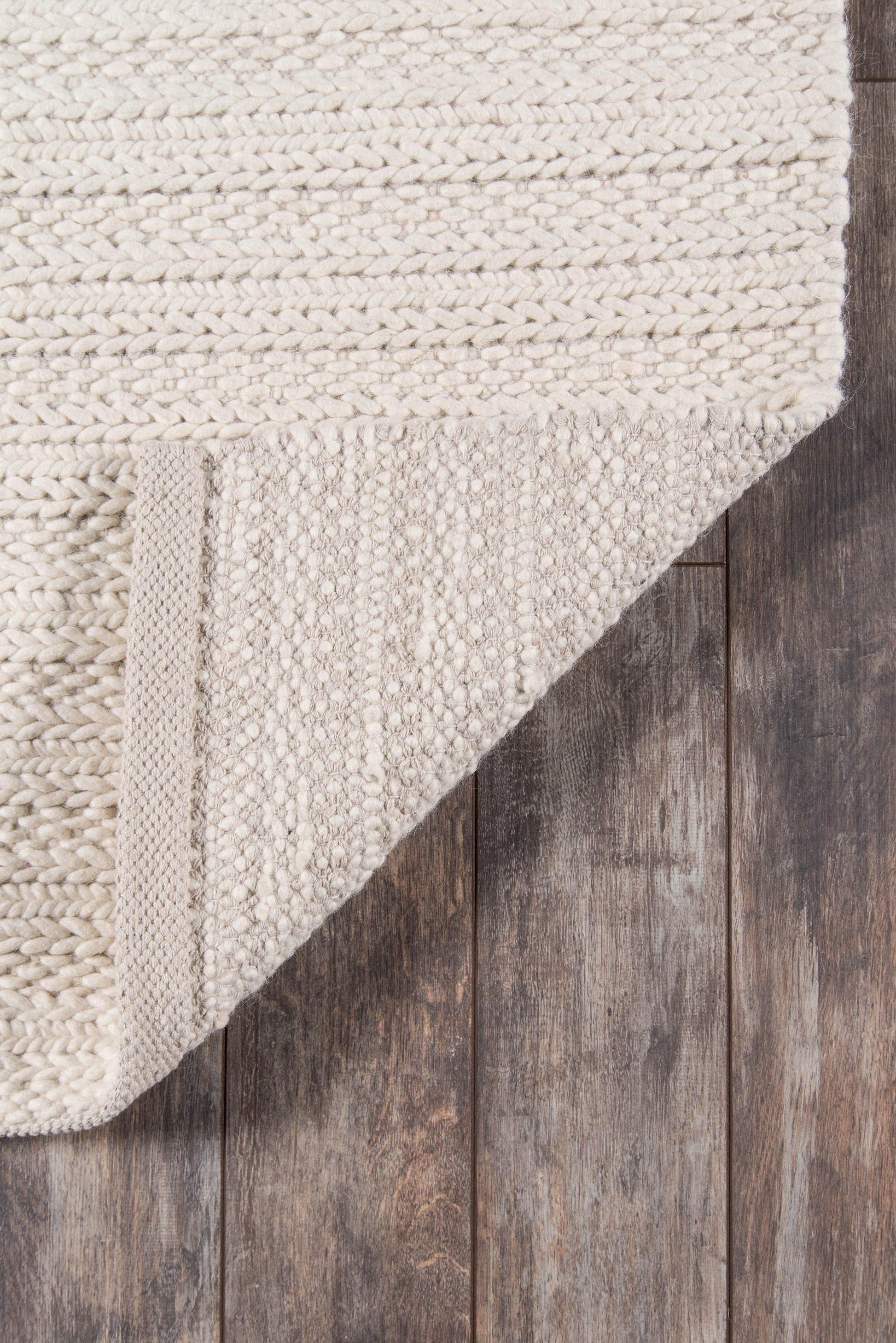 Cream woven rug with chunky braided texture, folded corner showing underside, on dark wood floor.