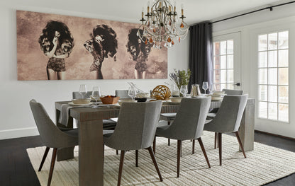 Grey upholstered dining chairs around a dark wood table with a crystal chandelier, sepia triptych wall art, and French doors.