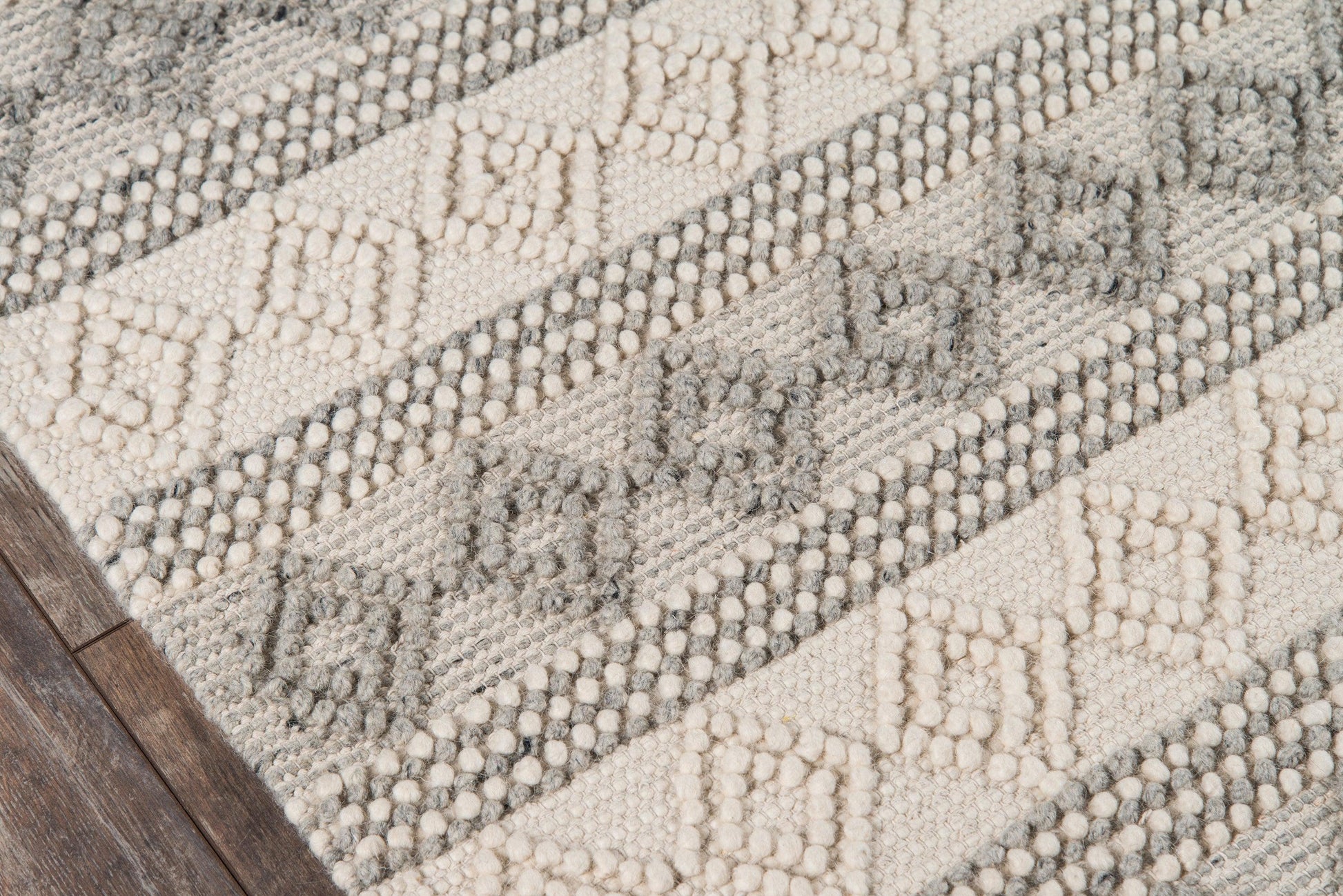 Ivory and gray geometric woven rug with diamond motifs, textured pile, rectangular rug on dark wood floor.