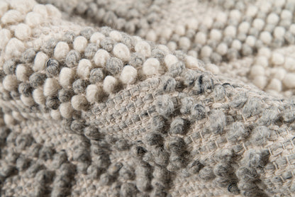 Macro shot of a soft ivory-gray boucle knit blanket with chunky, pom-pom-like textures.